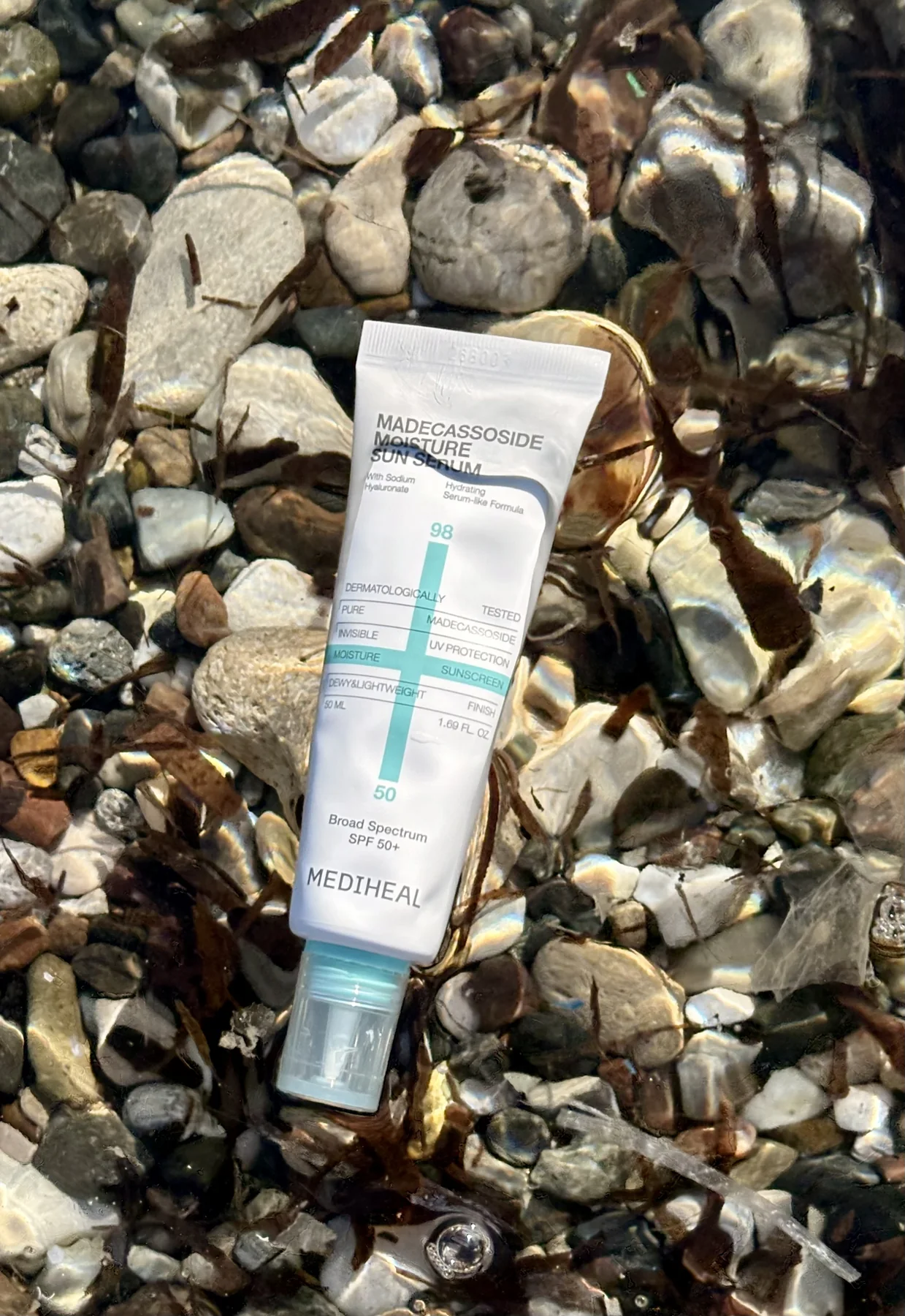 Mediheal skincare tube photographed among sunlit shells and stones